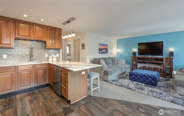 kitchen with pendant lighting, stainless steel dishwasher, open floor plan, a sink, and a peninsula