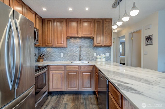 kitchen with appliances with stainless steel finishes, brown cabinetry, hanging light fixtures, and a sink