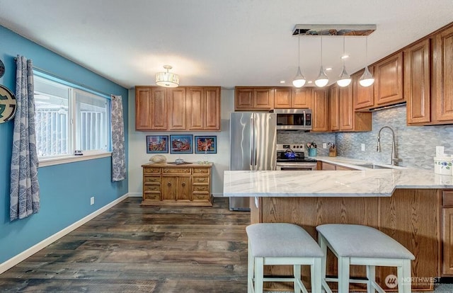 kitchen with hanging light fixtures, appliances with stainless steel finishes, a sink, light stone countertops, and a peninsula