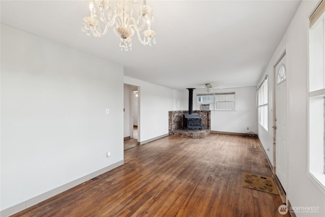 unfurnished living room featuring hardwood / wood-style flooring, a wood stove, and ceiling fan with notable chandelier