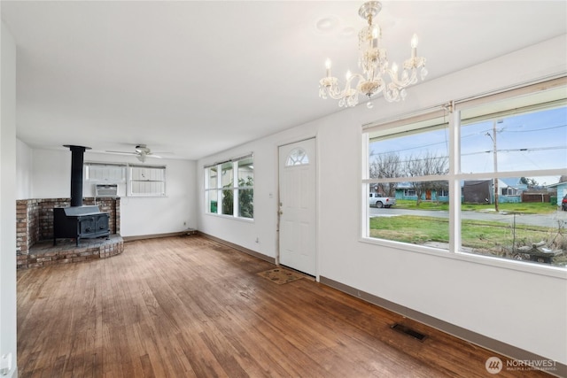 unfurnished living room with ceiling fan with notable chandelier, hardwood / wood-style floors, and a wood stove