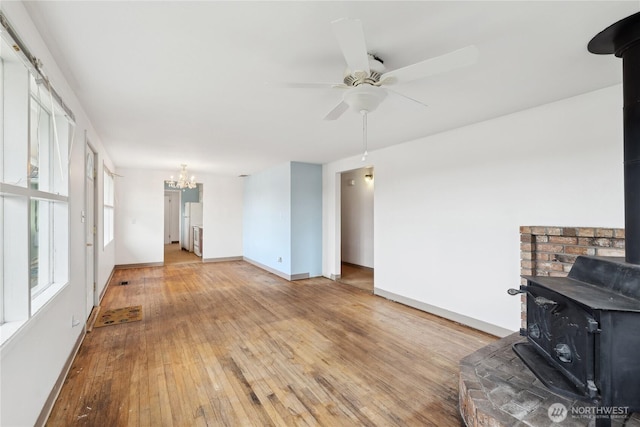 living room with a wood stove, ceiling fan with notable chandelier, and light hardwood / wood-style floors