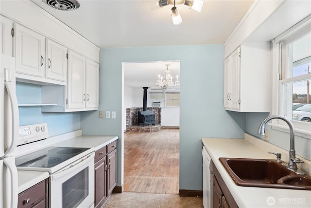 kitchen featuring sink, hanging light fixtures, a wood stove, white appliances, and white cabinets