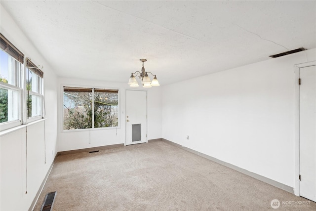 empty room with light colored carpet and a chandelier