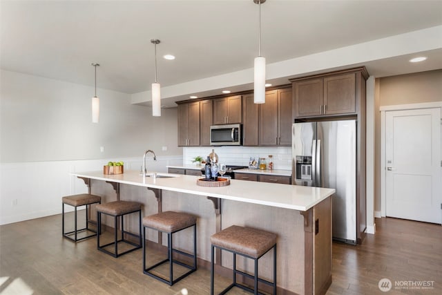 kitchen with stainless steel appliances, sink, pendant lighting, and a kitchen island with sink