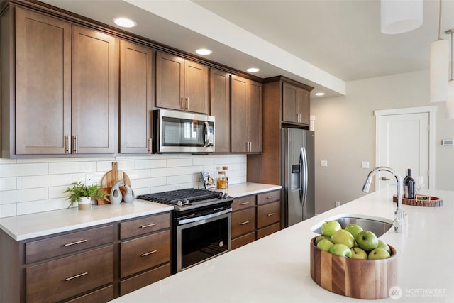 kitchen with dark brown cabinetry, sink, decorative light fixtures, stainless steel appliances, and backsplash