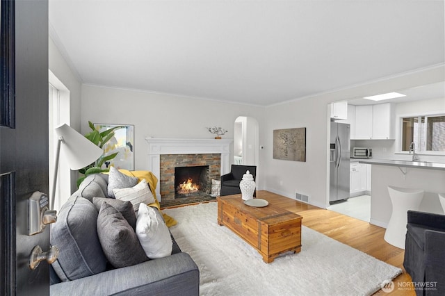 living room featuring crown molding, a stone fireplace, sink, and light wood-type flooring