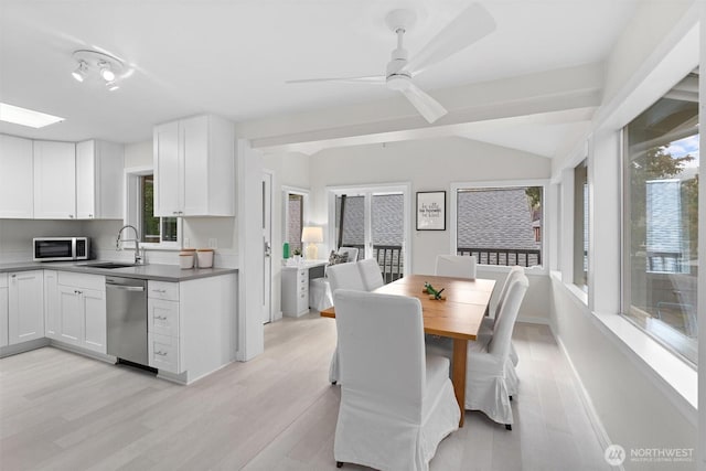 dining room featuring ceiling fan, sink, vaulted ceiling with skylight, and light hardwood / wood-style floors