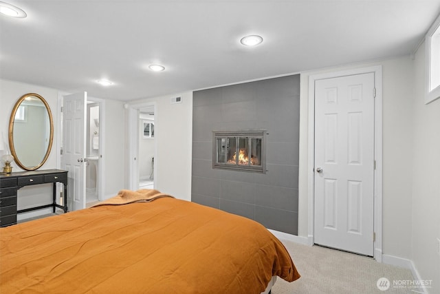 bedroom with a tiled fireplace, connected bathroom, and light colored carpet