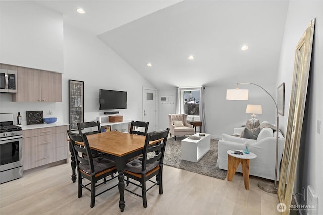 dining area with high vaulted ceiling and light hardwood / wood-style floors