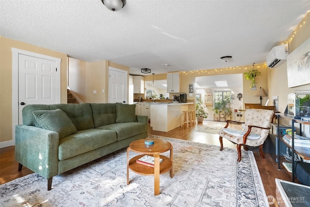 living room with a wall mounted AC, a textured ceiling, and light wood-type flooring