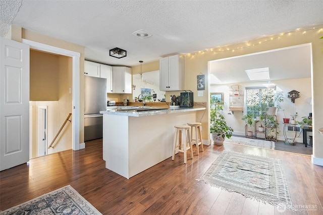 kitchen with stainless steel refrigerator, a breakfast bar area, white cabinets, kitchen peninsula, and dark wood-type flooring