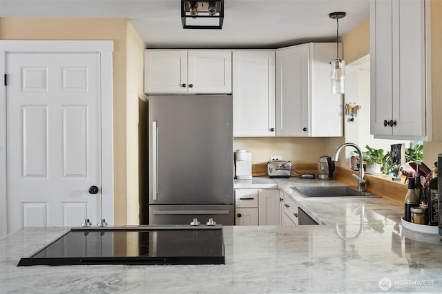 kitchen featuring white cabinetry, stainless steel fridge, light stone countertops, and sink