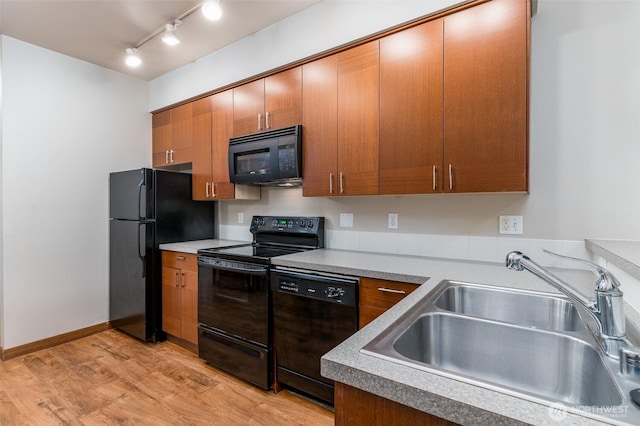 kitchen featuring baseboards, brown cabinetry, light wood-style flooring, black appliances, and a sink