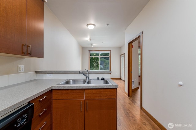 kitchen with dishwasher, a peninsula, light countertops, light wood-type flooring, and a sink