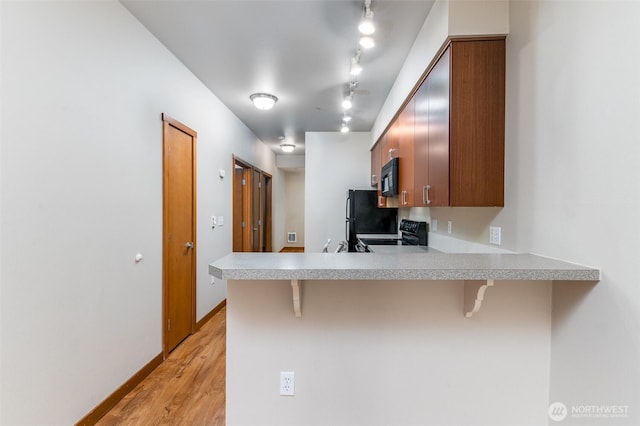 kitchen featuring a peninsula, black appliances, a kitchen breakfast bar, and light countertops