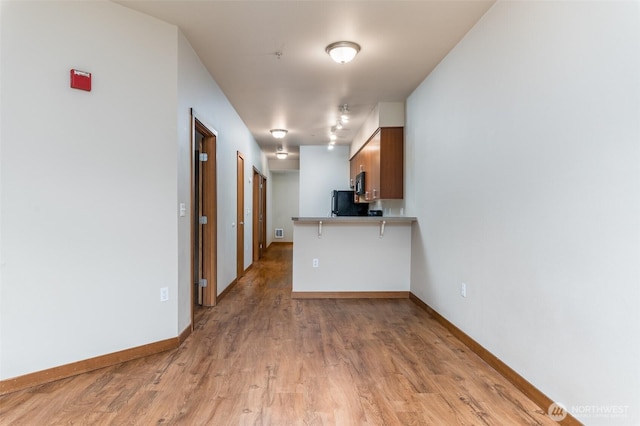 kitchen with brown cabinets, light wood finished floors, freestanding refrigerator, a peninsula, and baseboards