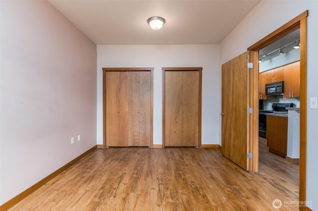 unfurnished bedroom featuring light wood-style flooring, baseboards, and multiple closets