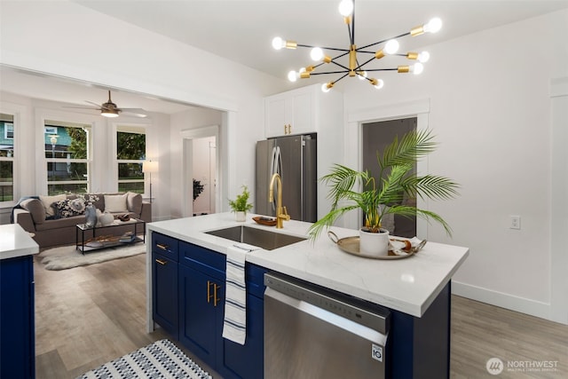 kitchen with an island with sink, sink, light stone counters, stainless steel appliances, and blue cabinetry