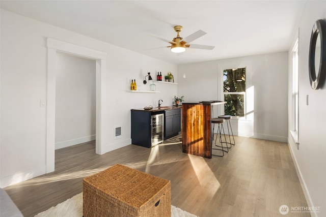 bar with wood-type flooring, beverage cooler, and ceiling fan