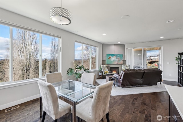 dining room with baseboards, visible vents, dark wood-type flooring, a lit fireplace, and recessed lighting