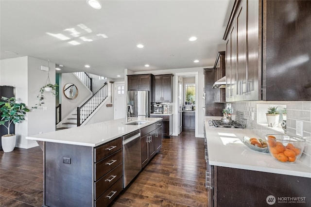 kitchen featuring a sink, light countertops, appliances with stainless steel finishes, an island with sink, and dark wood finished floors
