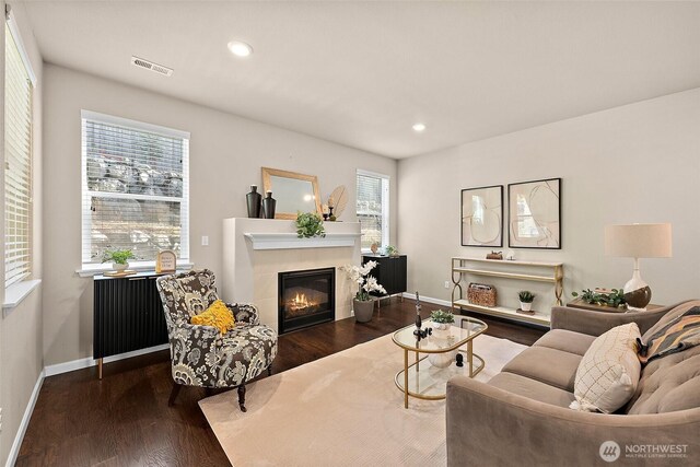 living room featuring a tiled fireplace and dark wood-type flooring