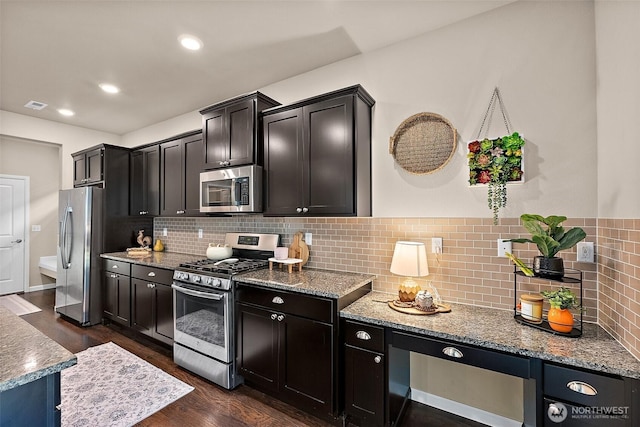 kitchen with dark wood-type flooring, appliances with stainless steel finishes, backsplash, and stone counters