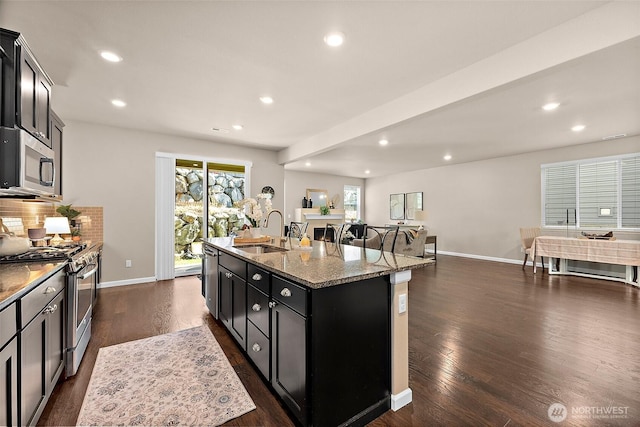 kitchen featuring dark wood-type flooring, sink, appliances with stainless steel finishes, an island with sink, and light stone countertops