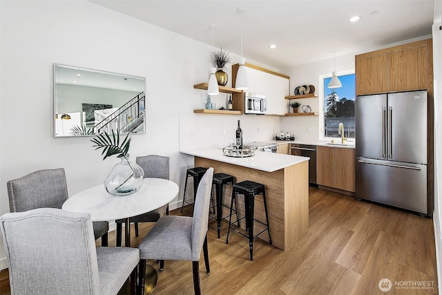 kitchen with sink, decorative light fixtures, light wood-type flooring, appliances with stainless steel finishes, and kitchen peninsula