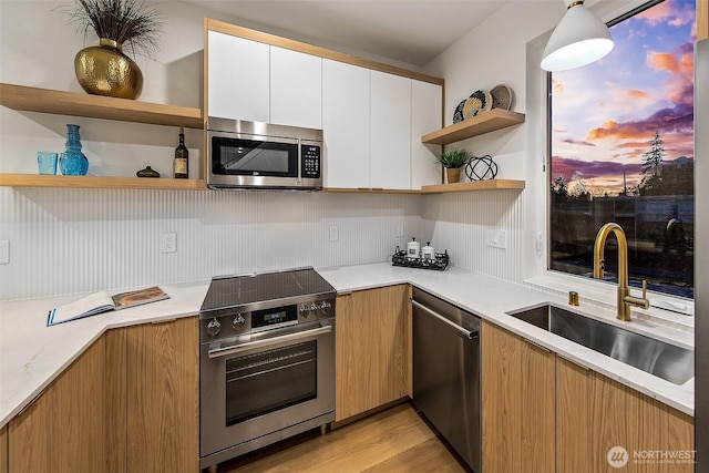 kitchen featuring white cabinetry, sink, hanging light fixtures, light stone counters, and stainless steel appliances