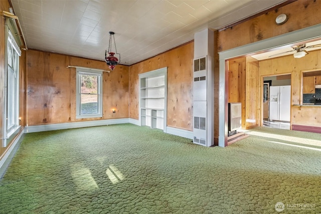 carpeted spare room with ceiling fan, wooden walls, and built in features