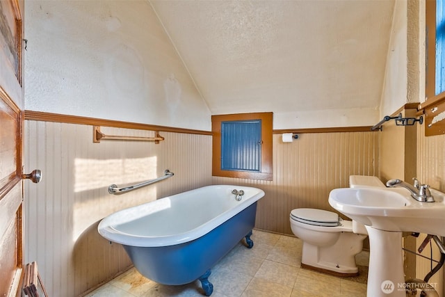 bathroom with a washtub, wooden walls, a textured ceiling, vaulted ceiling, and toilet