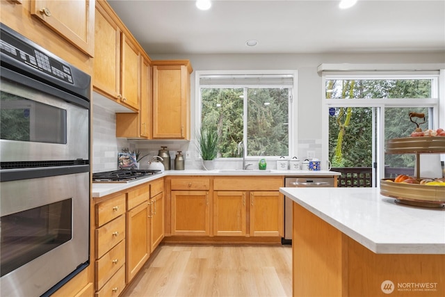 kitchen featuring appliances with stainless steel finishes, sink, light hardwood / wood-style flooring, and decorative backsplash