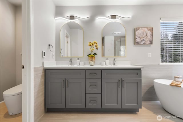 bathroom featuring a washtub, toilet, tile walls, wood-type flooring, and vanity