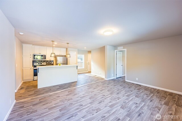 kitchen with white cabinets, open floor plan, a center island, stainless steel appliances, and light countertops