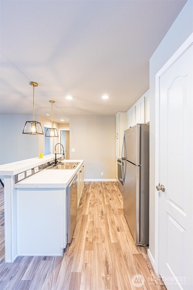 kitchen featuring white cabinets, decorative light fixtures, stainless steel appliances, light countertops, and a sink