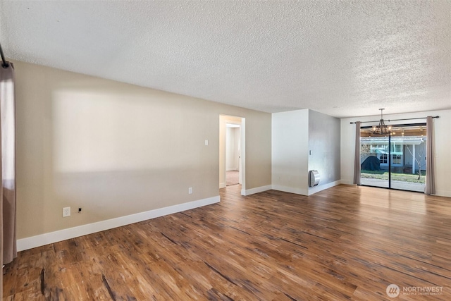 empty room with a textured ceiling, wood finished floors, baseboards, and a chandelier