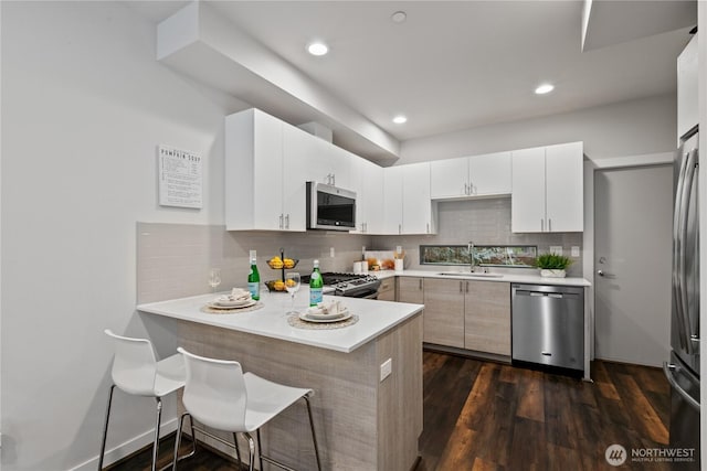 kitchen featuring appliances with stainless steel finishes, sink, white cabinets, kitchen peninsula, and dark wood-type flooring