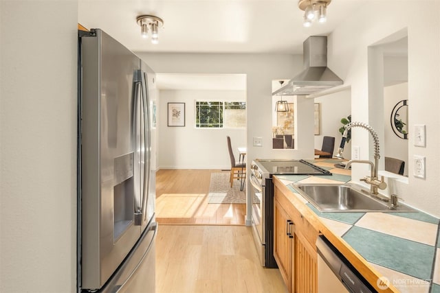 kitchen featuring sink, light hardwood / wood-style floors, stainless steel appliances, and wall chimney exhaust hood