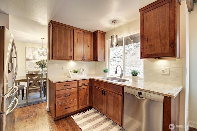 kitchen with appliances with stainless steel finishes, dark hardwood / wood-style floors, pendant lighting, sink, and light stone counters