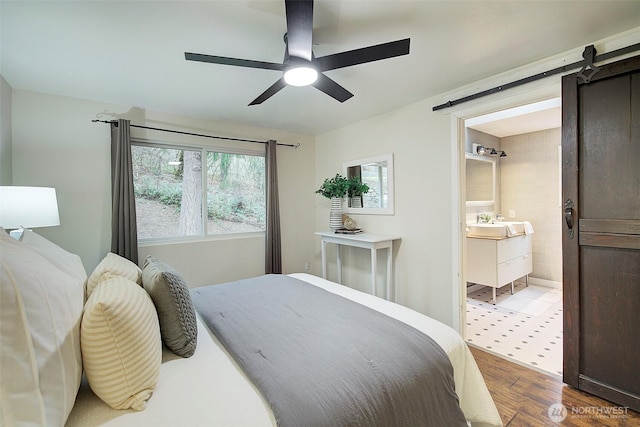 bedroom with hardwood / wood-style floors, sink, ceiling fan, a barn door, and ensuite bath