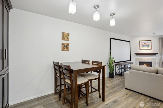 dining area with light wood-style floors, baseboards, and a tiled fireplace