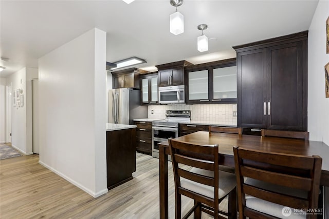 kitchen with decorative light fixtures, stainless steel appliances, light wood-style floors, backsplash, and glass insert cabinets