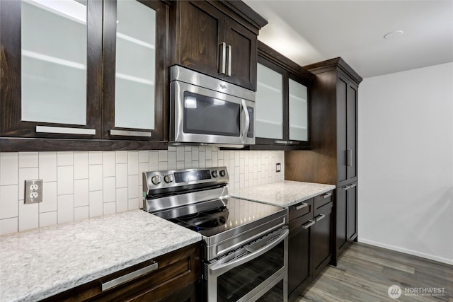 kitchen with appliances with stainless steel finishes, glass insert cabinets, and decorative backsplash