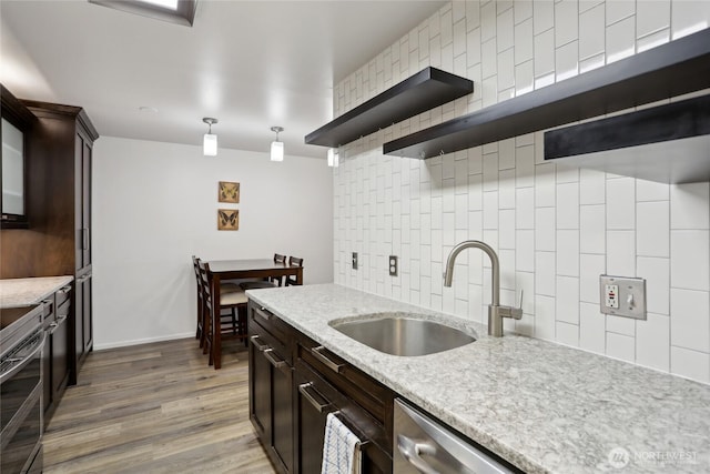 kitchen featuring open shelves, tasteful backsplash, light stone countertops, pendant lighting, and a sink