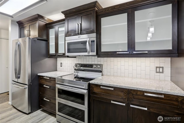 kitchen featuring light stone counters, appliances with stainless steel finishes, backsplash, and glass insert cabinets