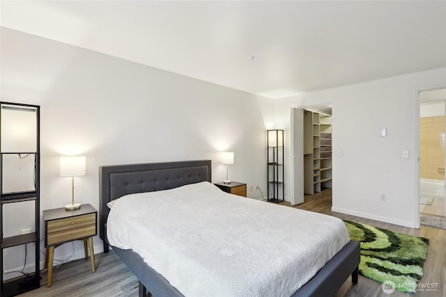 bedroom featuring wood finished floors, baseboards, a spacious closet, a closet, and ensuite bath