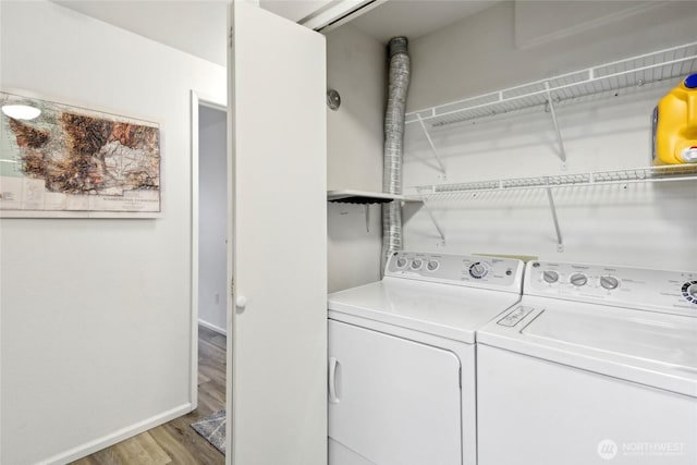 clothes washing area with laundry area, baseboards, washer and dryer, and wood finished floors