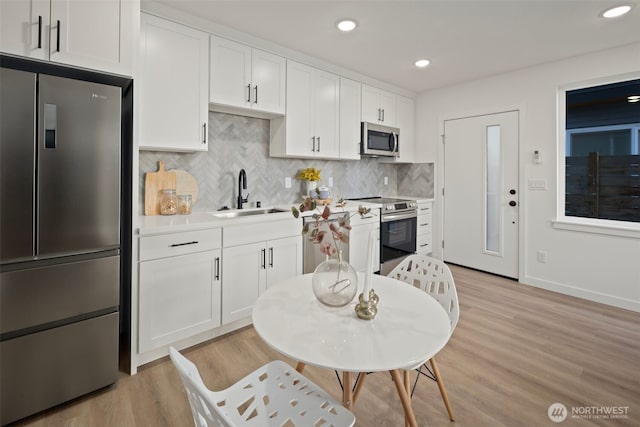 kitchen with appliances with stainless steel finishes, sink, white cabinets, backsplash, and light hardwood / wood-style flooring